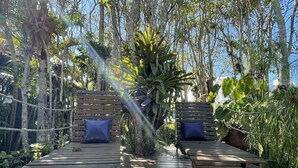 A wooden deck with two lounge chairs, each with a pillow. The deck is surrounded by dense tropical foliage and trees. - Casa Jardim Bangalôs (Paraty)