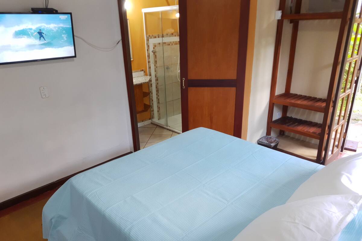 A room with a bed, a television mounted on the wall, a wooden door, and a small shelf.