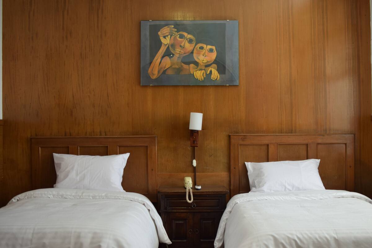 Une chambre d’hôtel avec deux lits, des têtes de lit en bois, un tableau au mur et un téléphone sur la table de chevet.
