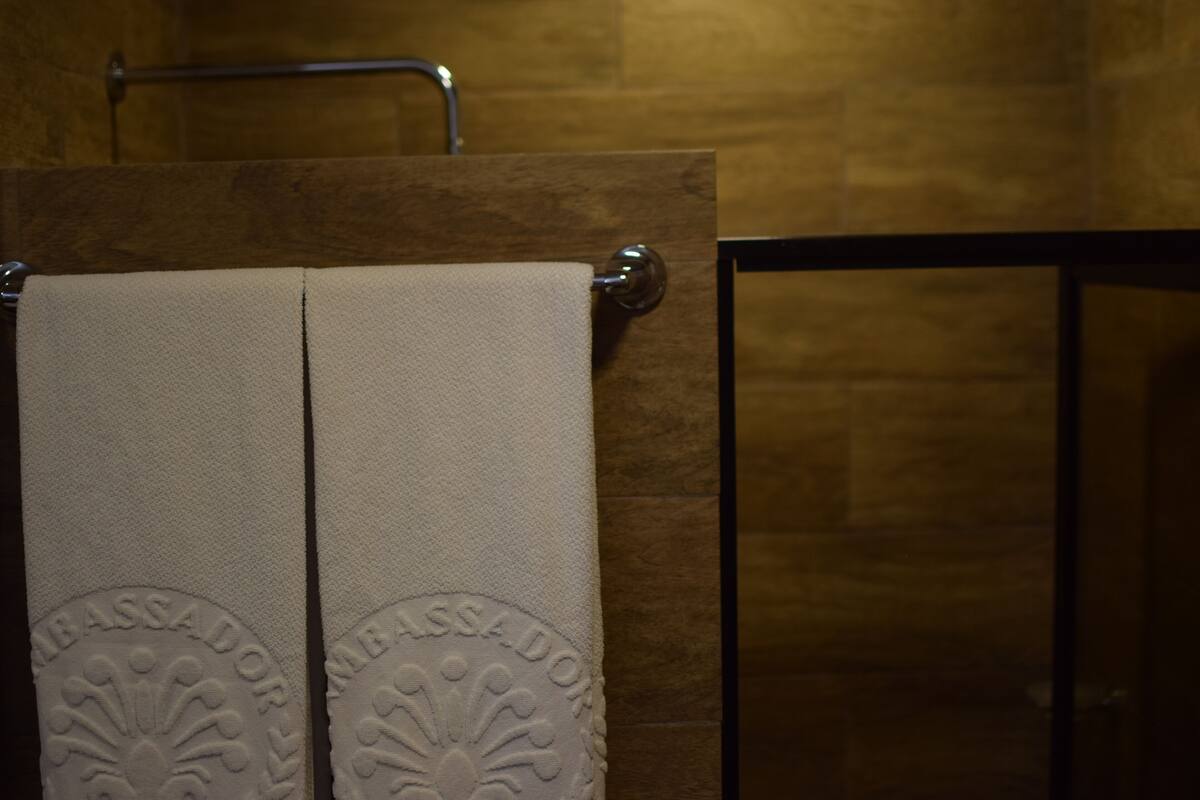 Une salle de bain avec un porte-serviettes sur lequel sont posées deux serviettes, un mur en bois et une porte de douche en verre.