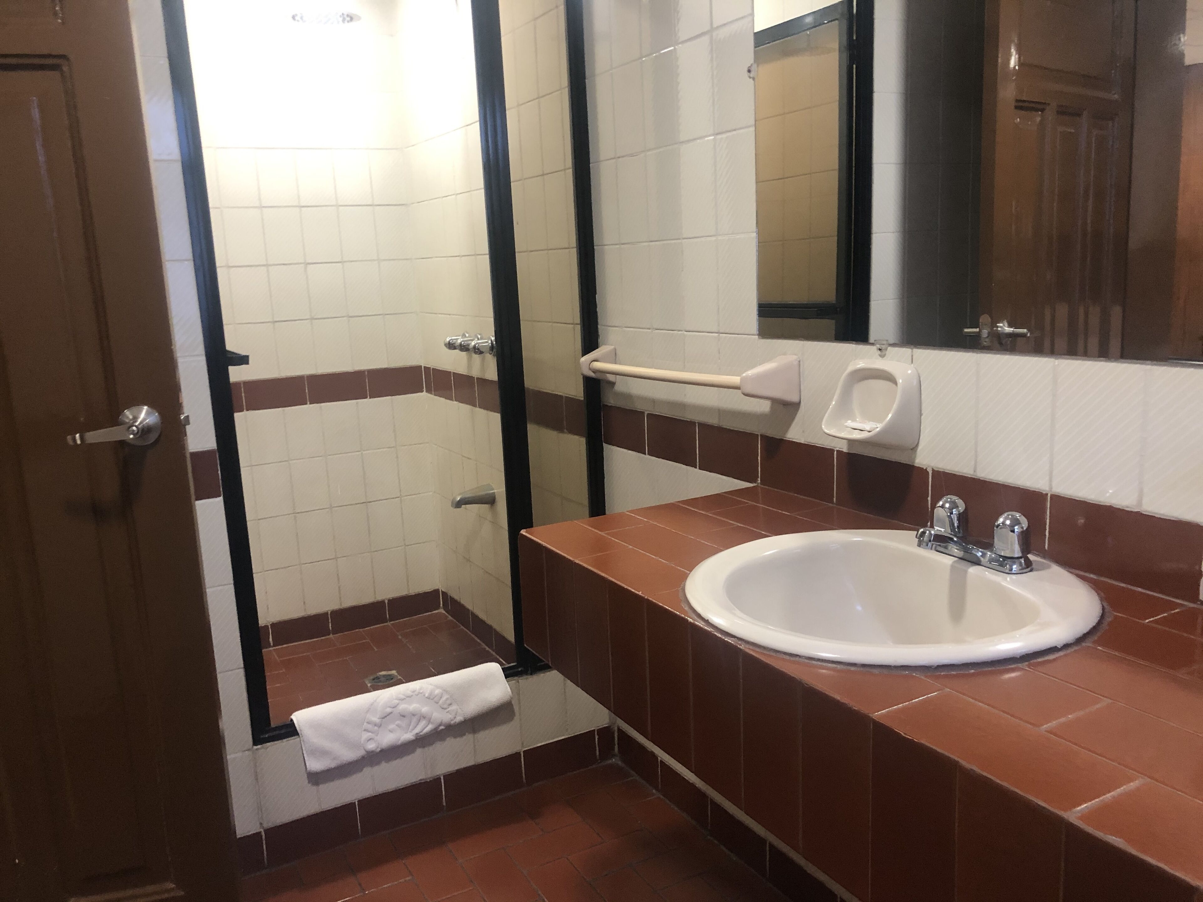 Un baño con un lavamanos blanco, baldosas marrones, un perchero y un espejo.