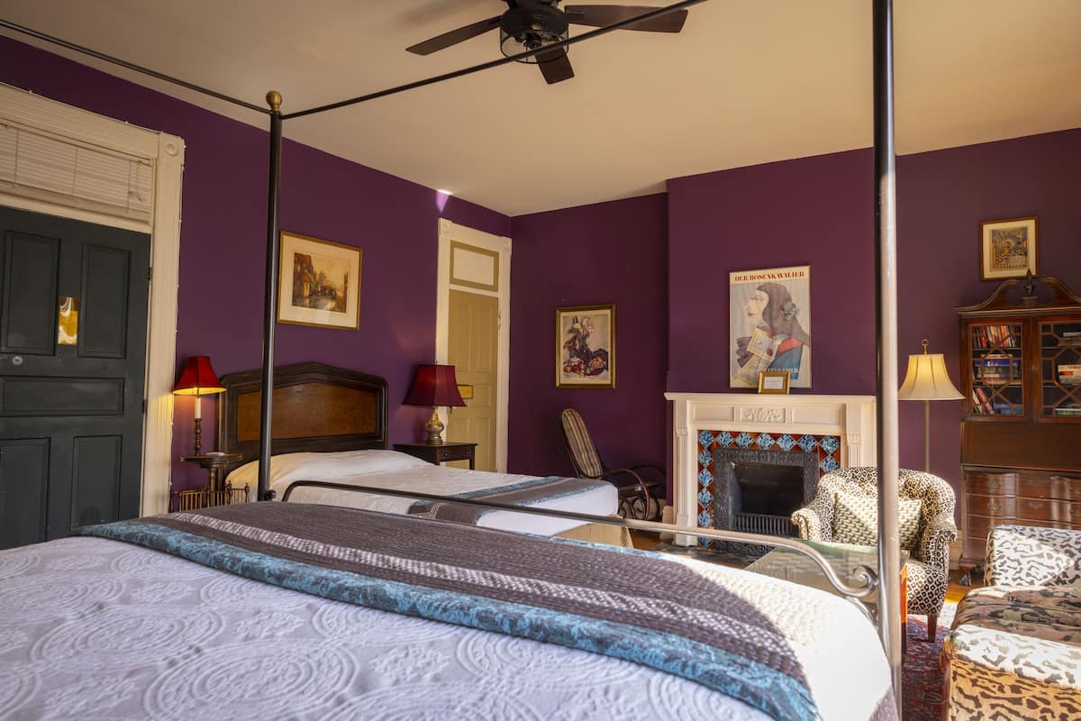 A bedroom with two beds, a fireplace, and a bookshelf.