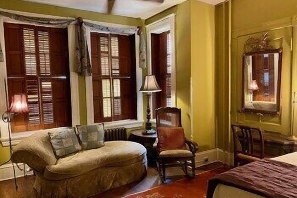 A room with a sofa, a chair, a lamp, and a bed.