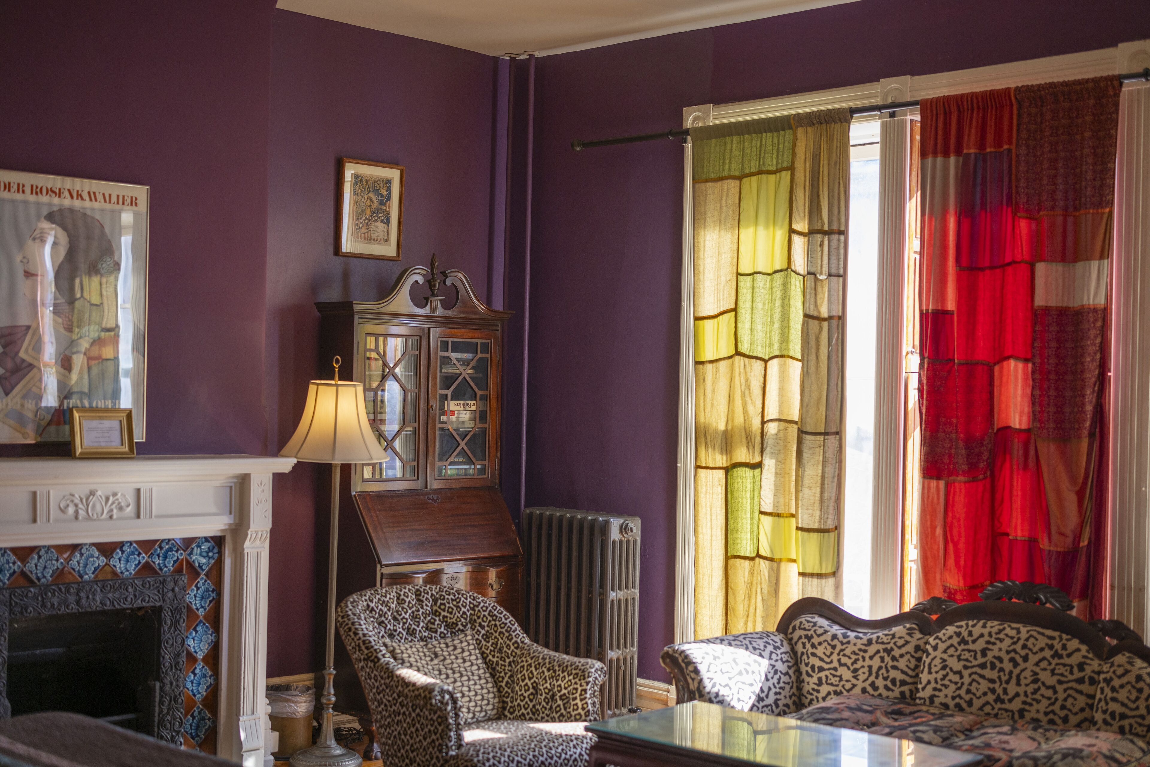 Una habitación con chimenea, sillones con estampado, una mesa y un ventanal con cortinas coloridas.
