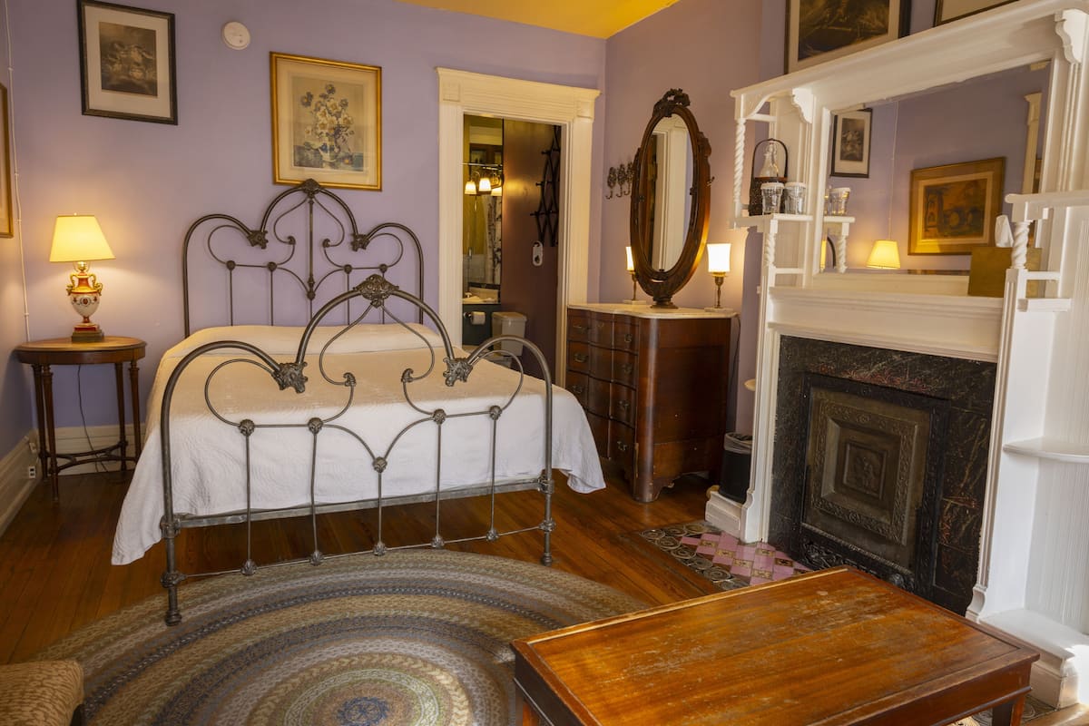 A bedroom with a metal bed frame, a wooden dresser, a fireplace, and a round rug.
