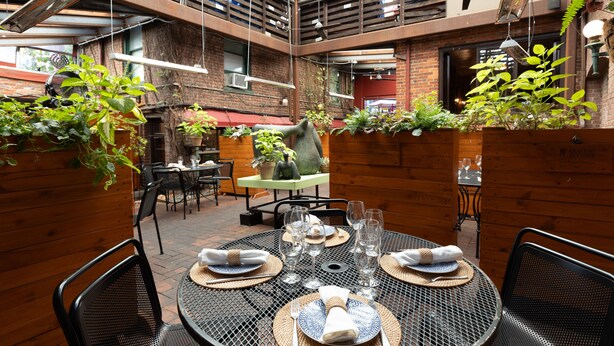 A restaurant with round metal tables set for dining, surrounded by wooden walls and hanging plants.