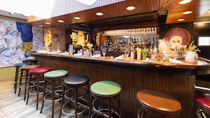 A bar area with stools, a counter, and a variety of bottles.