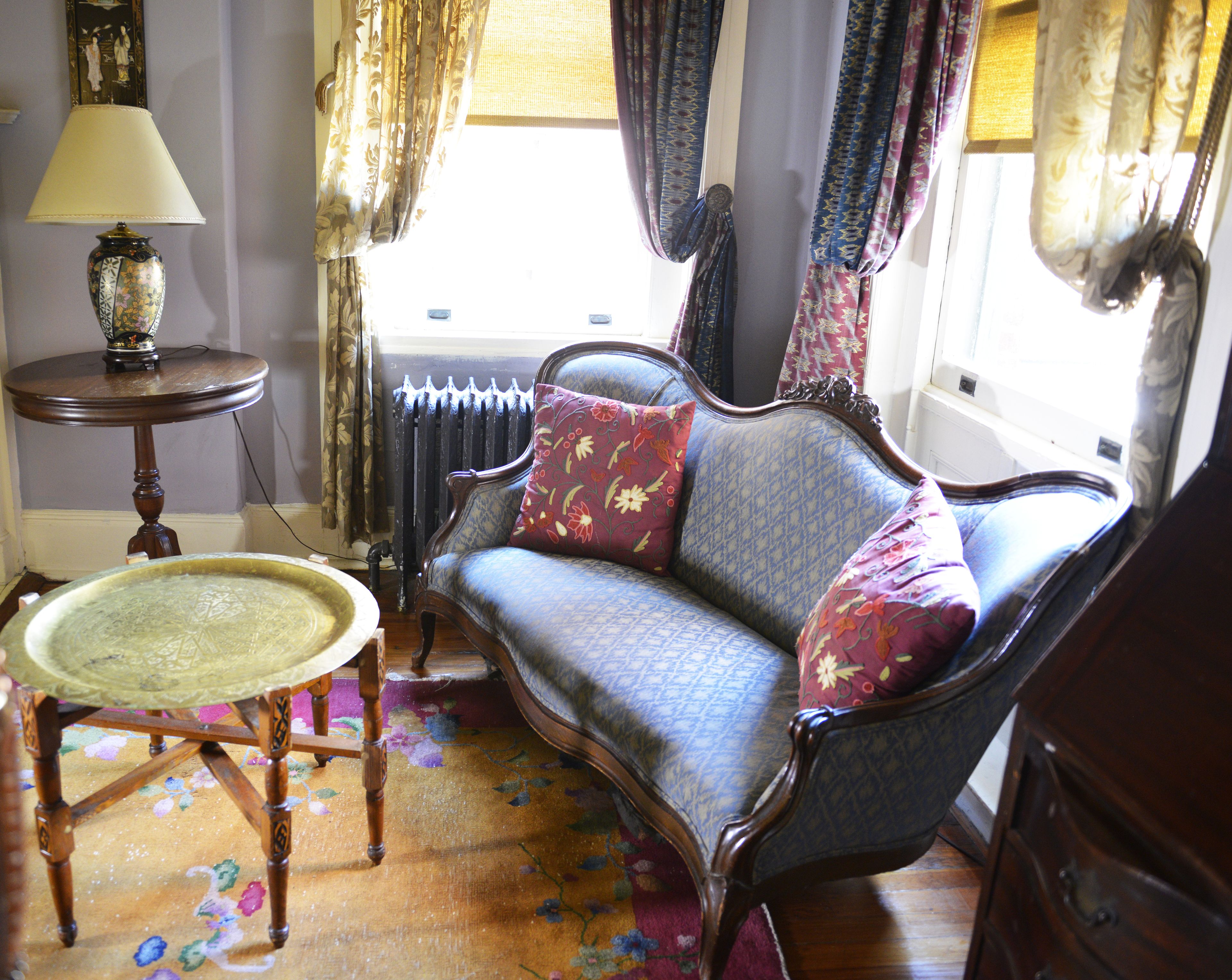 Una habitación de estilo vintage con un sofá estampado, una mesita redonda y un radiador.