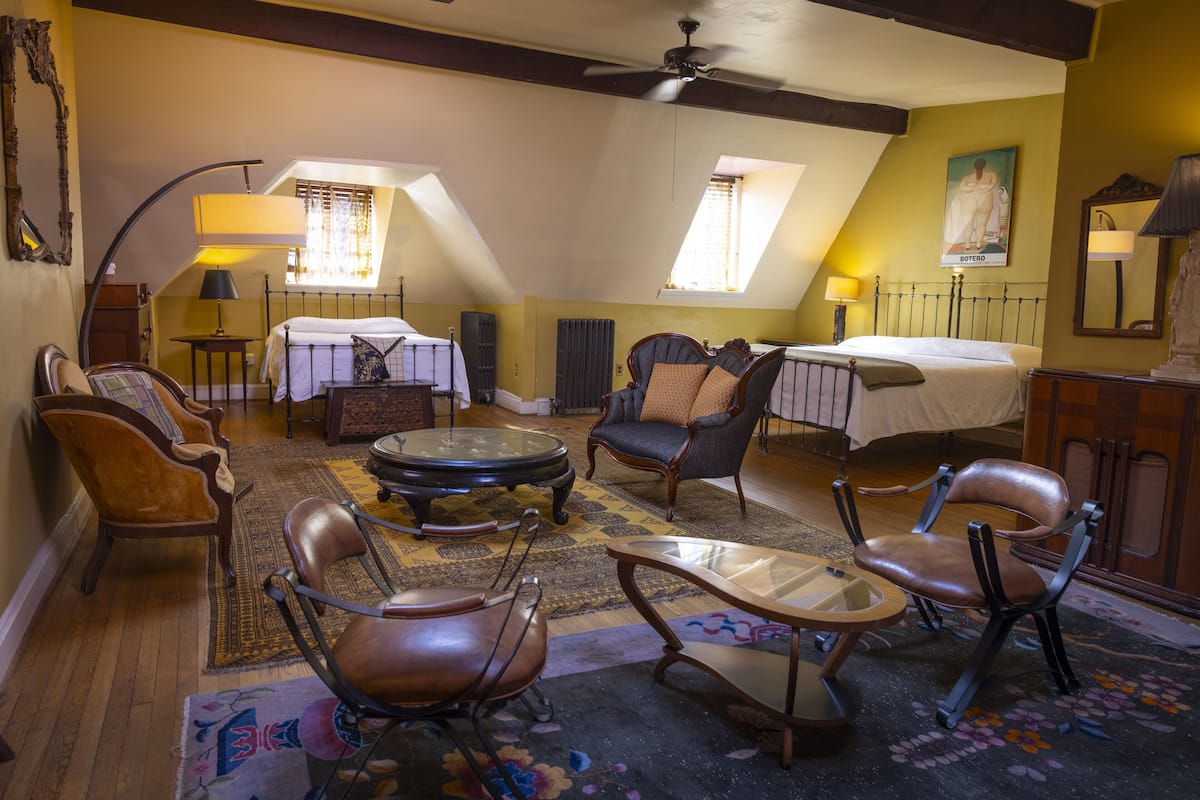 A cozy, well-lit room with a bed, a round coffee table, leather chairs, and a small table with a lamp.