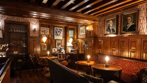 A cozy bar area with wooden paneling, framed artwork, and a variety of seating options including a bench and tables.