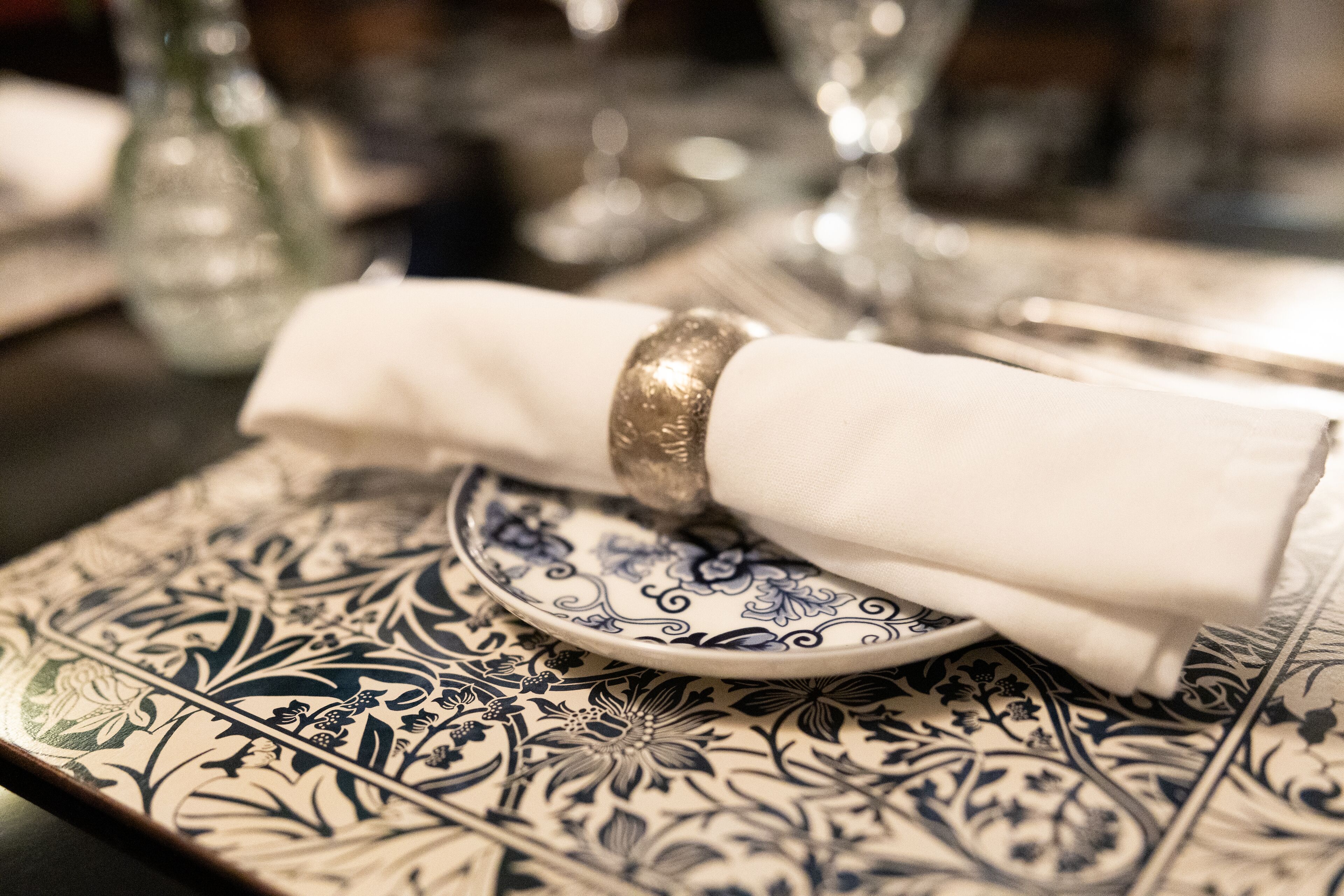 Una mesa dispuesta con una servilleta blanca, un anillo dorado y un plato con diseño azul y blanco.