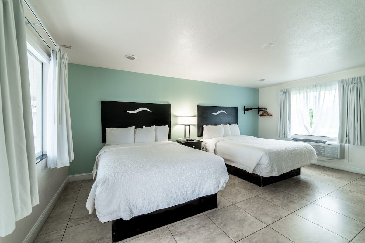 Een hotelkamer met twee bedden, een nachtkastje, een lamp en een raam met gordijnen.