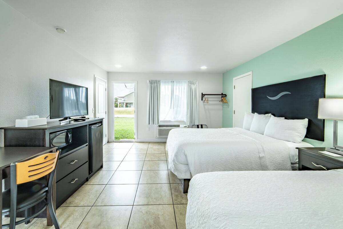 Een hotelkamer met twee bedden, een bureau met stoel, een televisie en uitzicht op de omgeving.