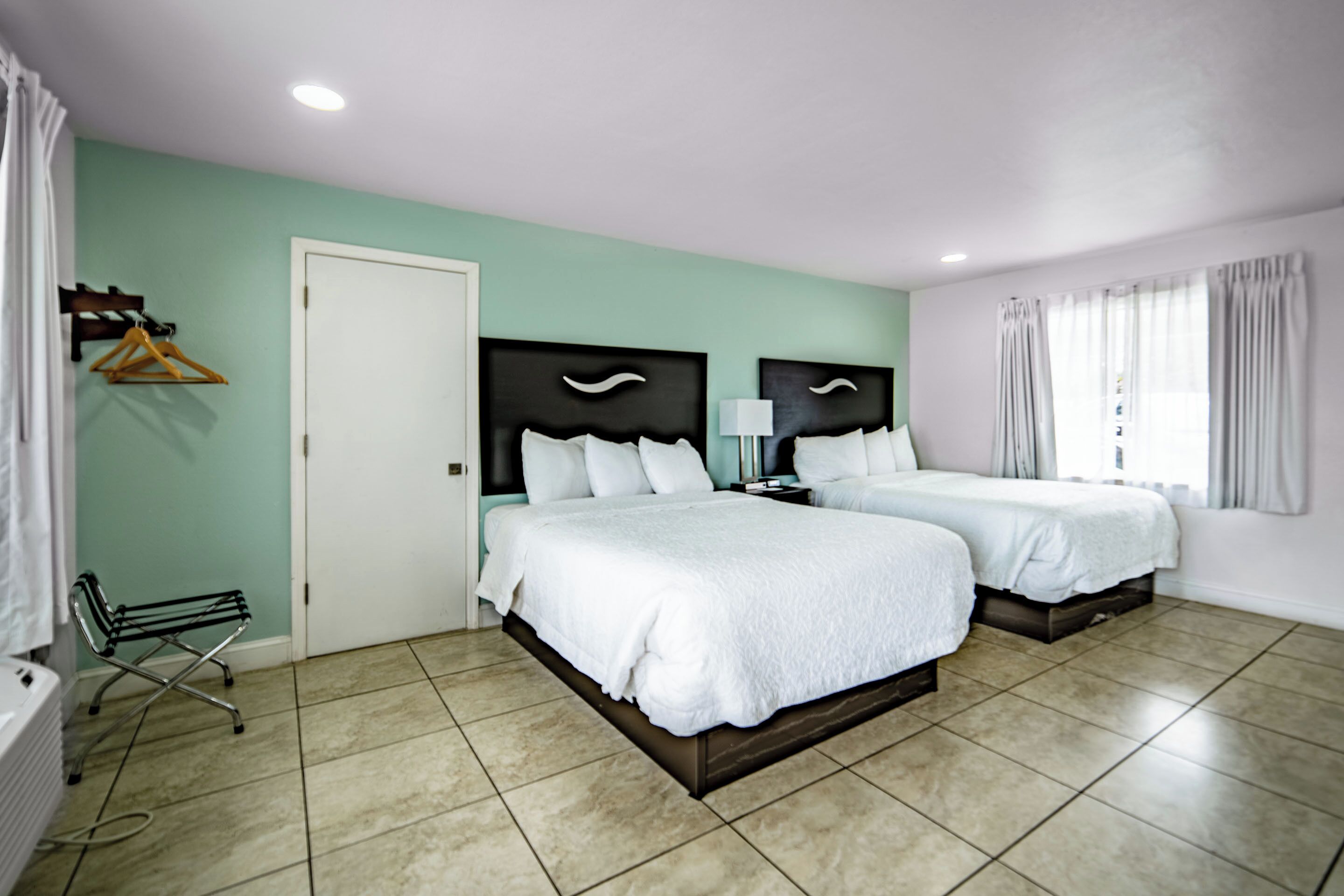 Une chambre d’hôtel avec deux lits, une salle de bain et une fenêtre avec des rideaux.