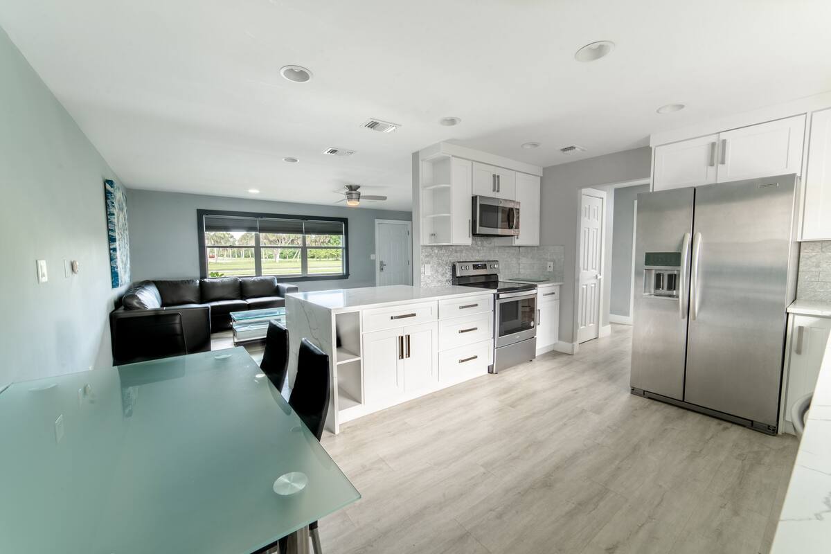 Een moderne keuken met witte kasten, roestvrijstalen apparatuur en een glazen eettafel.