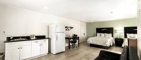 A compact hotel room with a kitchenette, a bed, a desk, and a sofa.