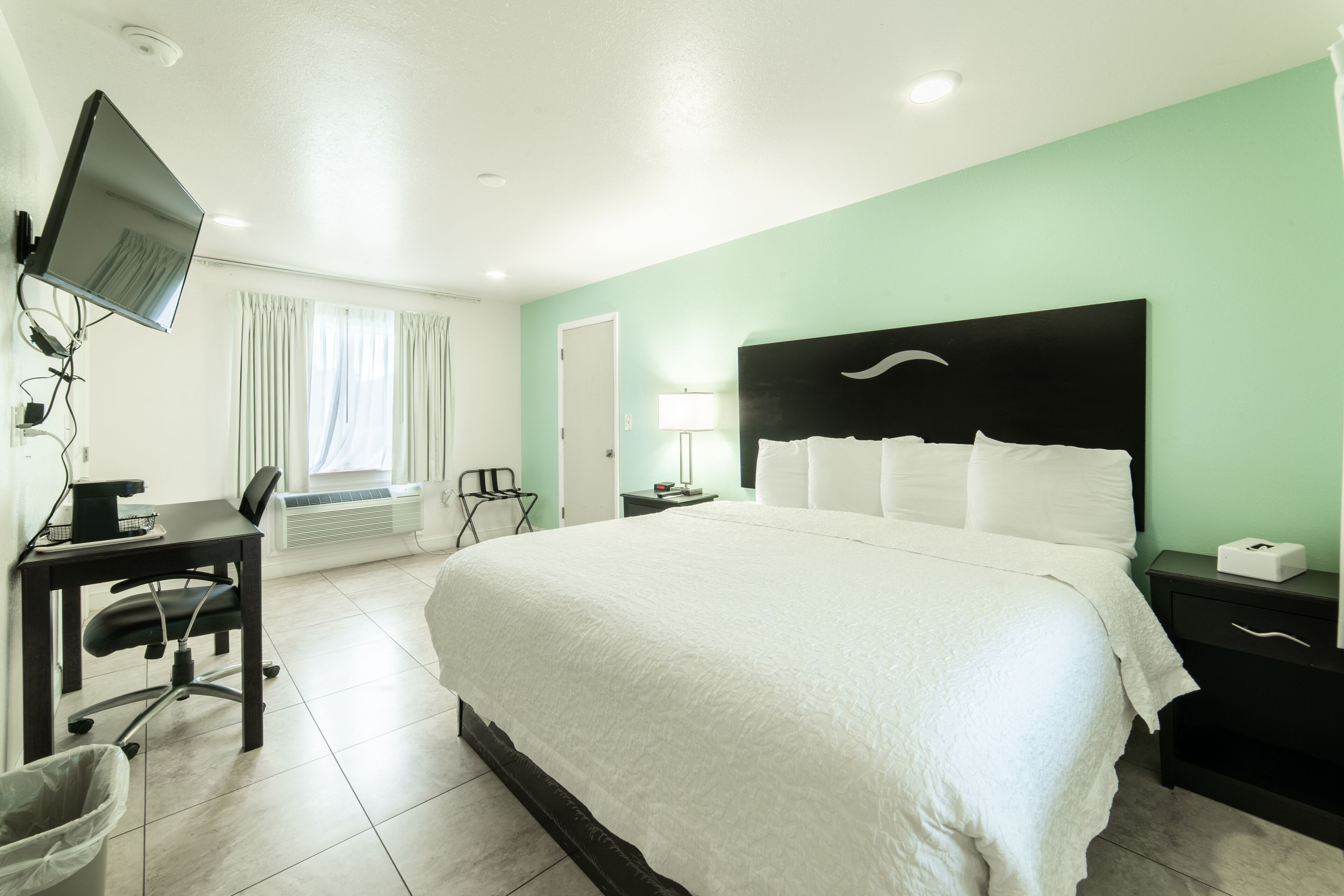 A hotel room with a large bed, a desk with a computer, a chair, and a TV mounted on the wall.