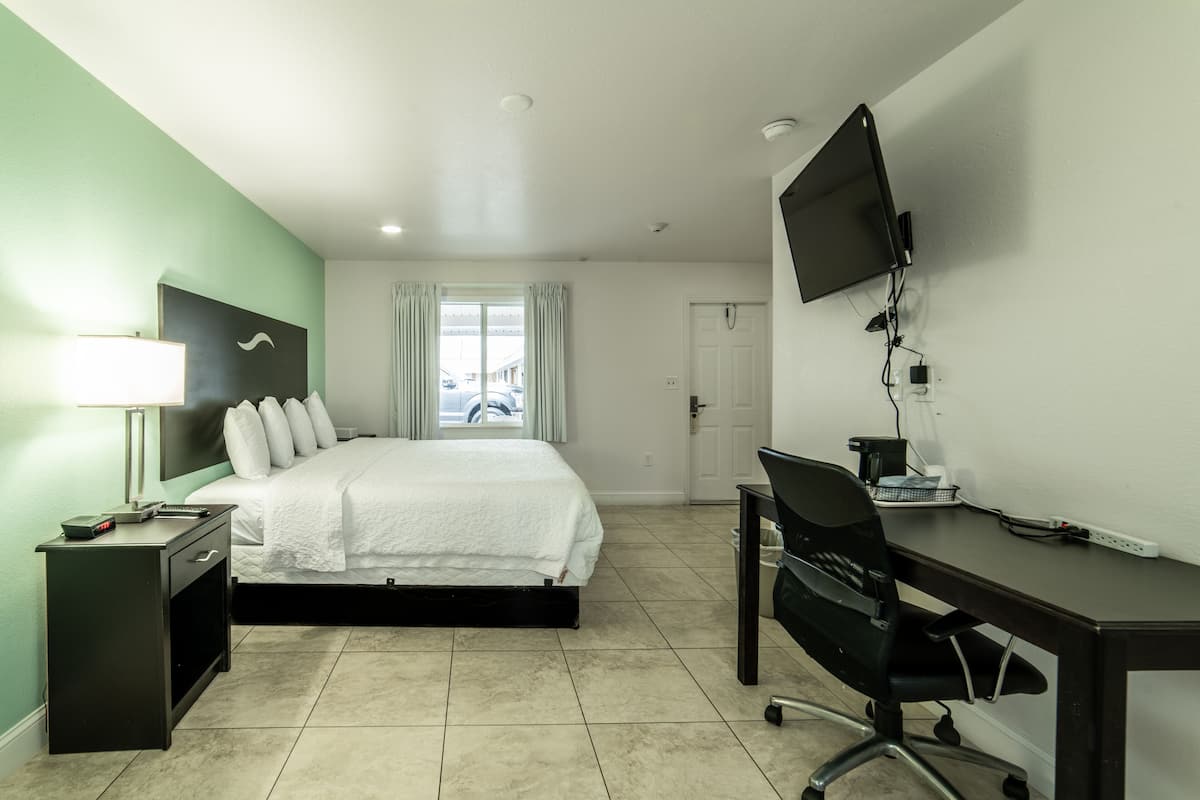 Een hotelkamer met een bed, bureau, stoel, televisie en een raam met gordijnen.