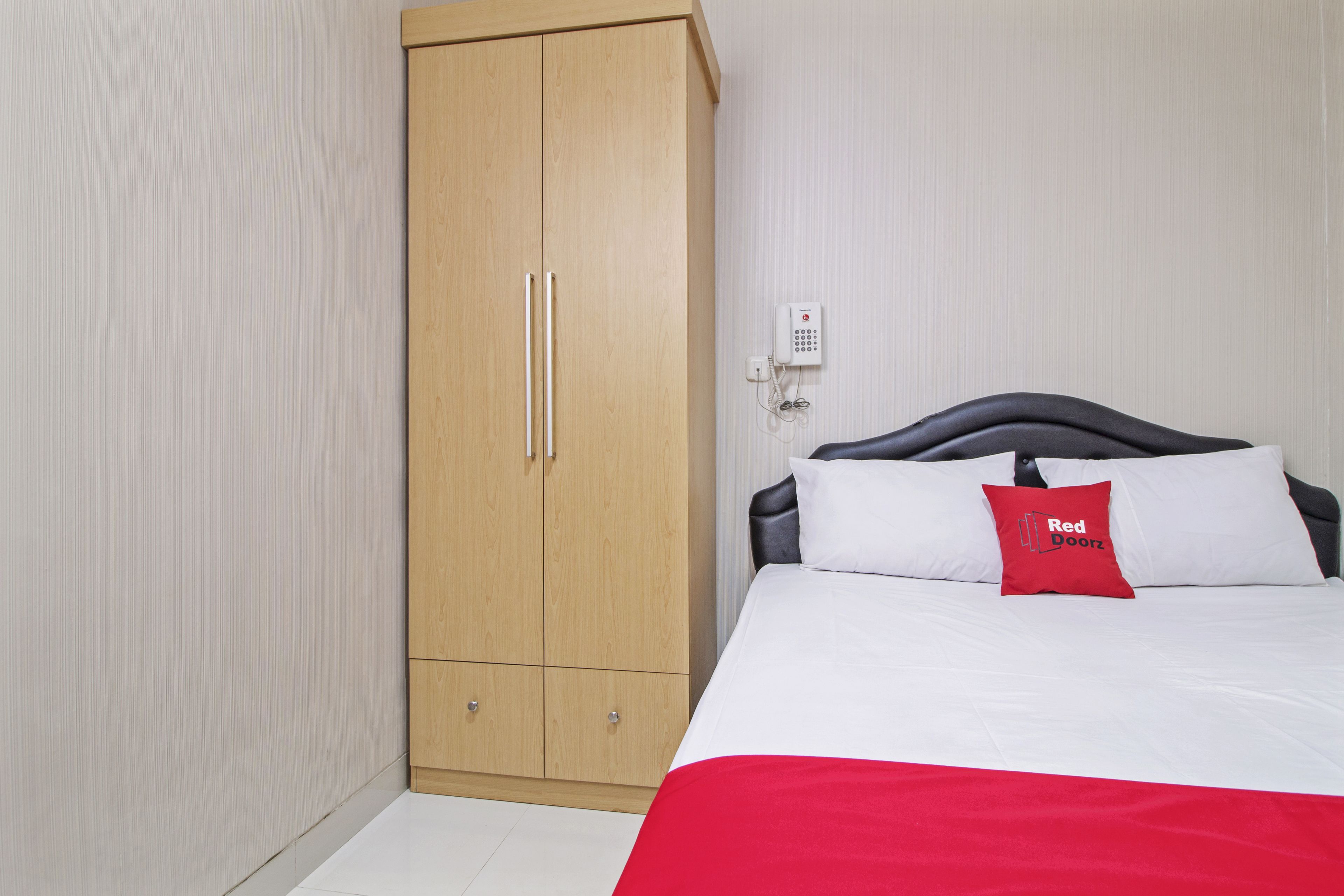 A bedroom with a bed, a wardrobe, and a wall-mounted phone.