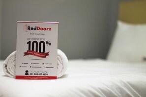 A rolled white towel on a bed with a RedDoorz promotional sign.