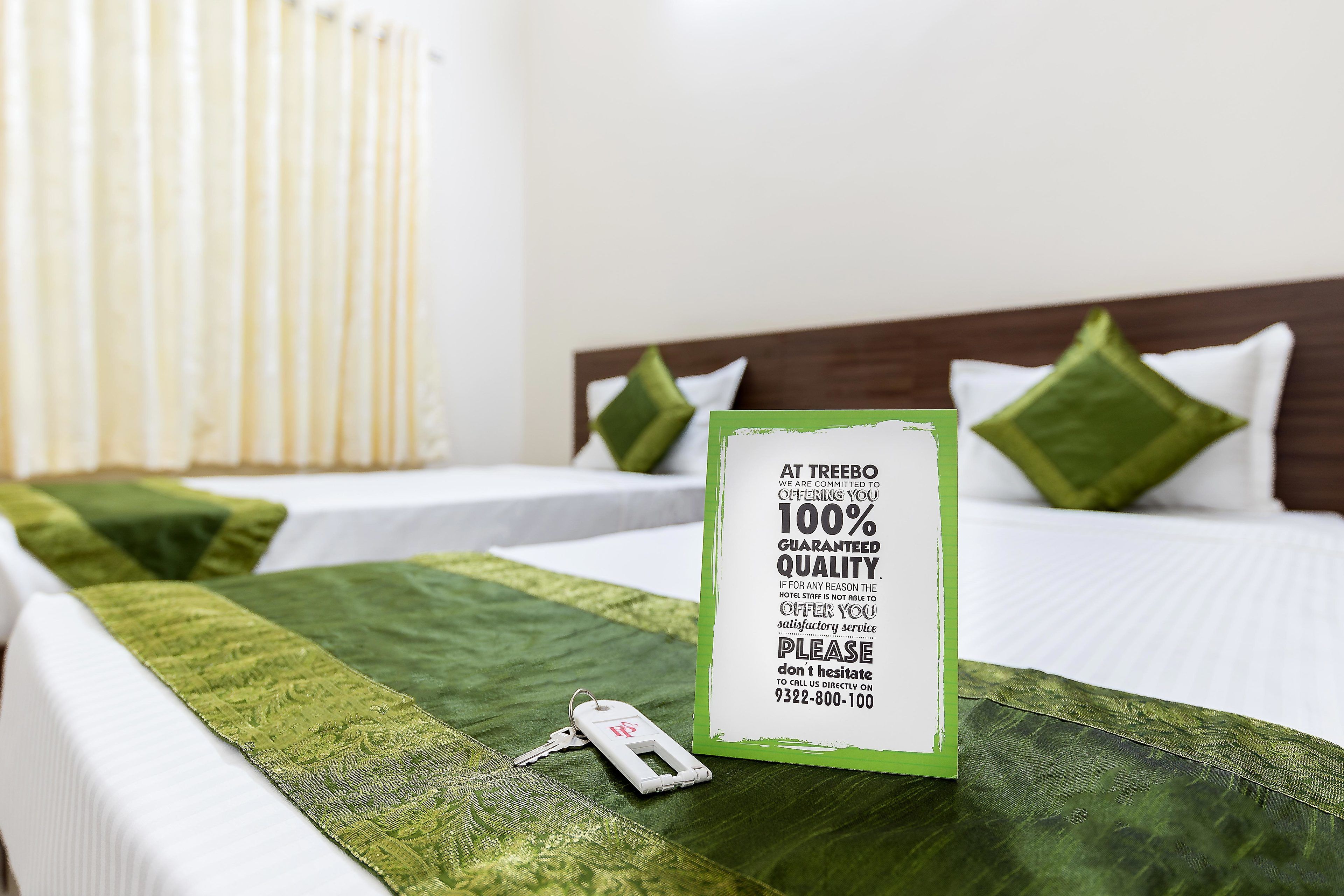 Een hotelkamer met twee bedden, groene dekbedden en een bord met daarop 100% gegarandeerde kwaliteitsservice.