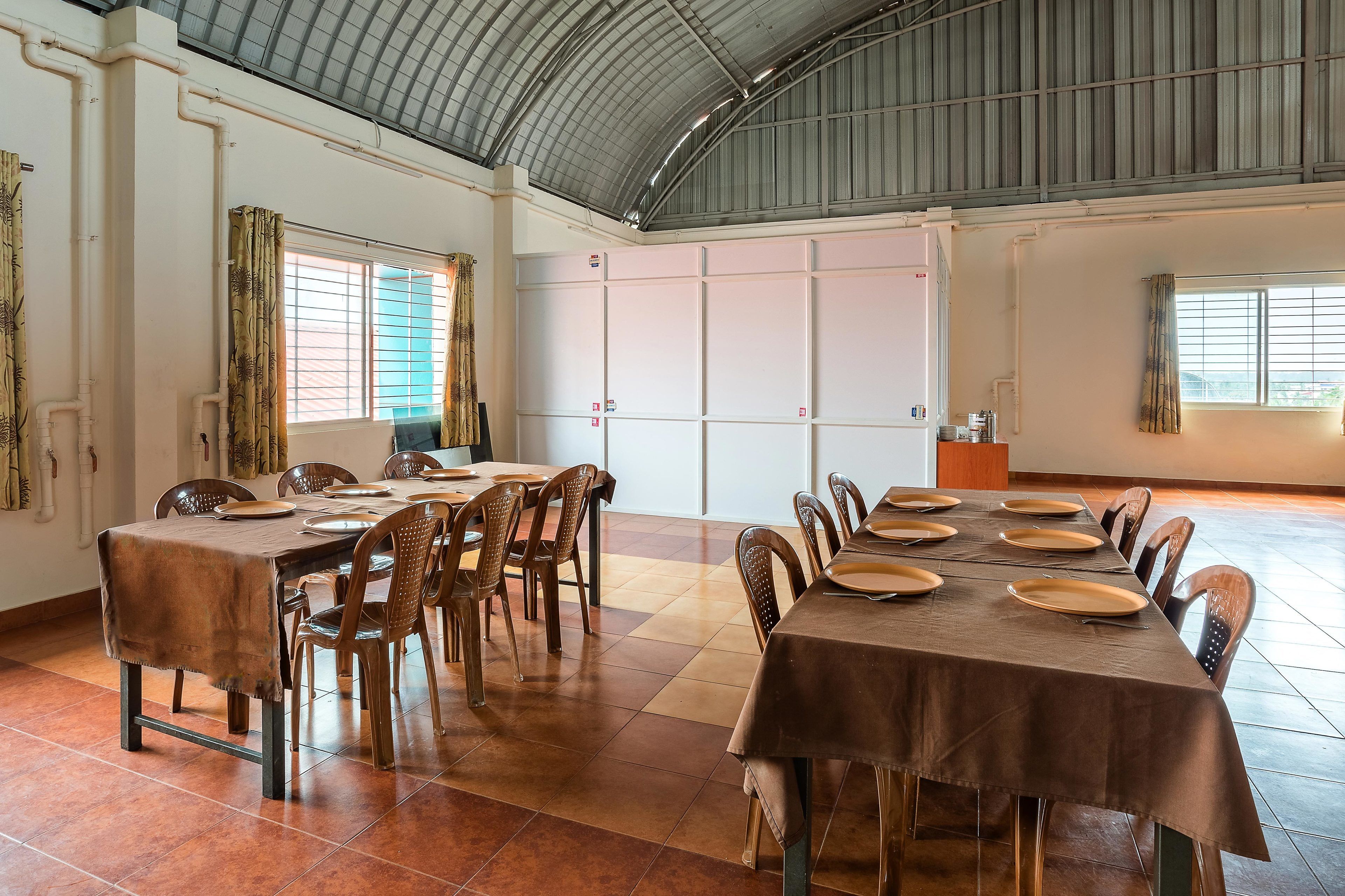Een ruime eetruimte met hoge plafonds en grote ramen, met meerdere tafels en stoelen.