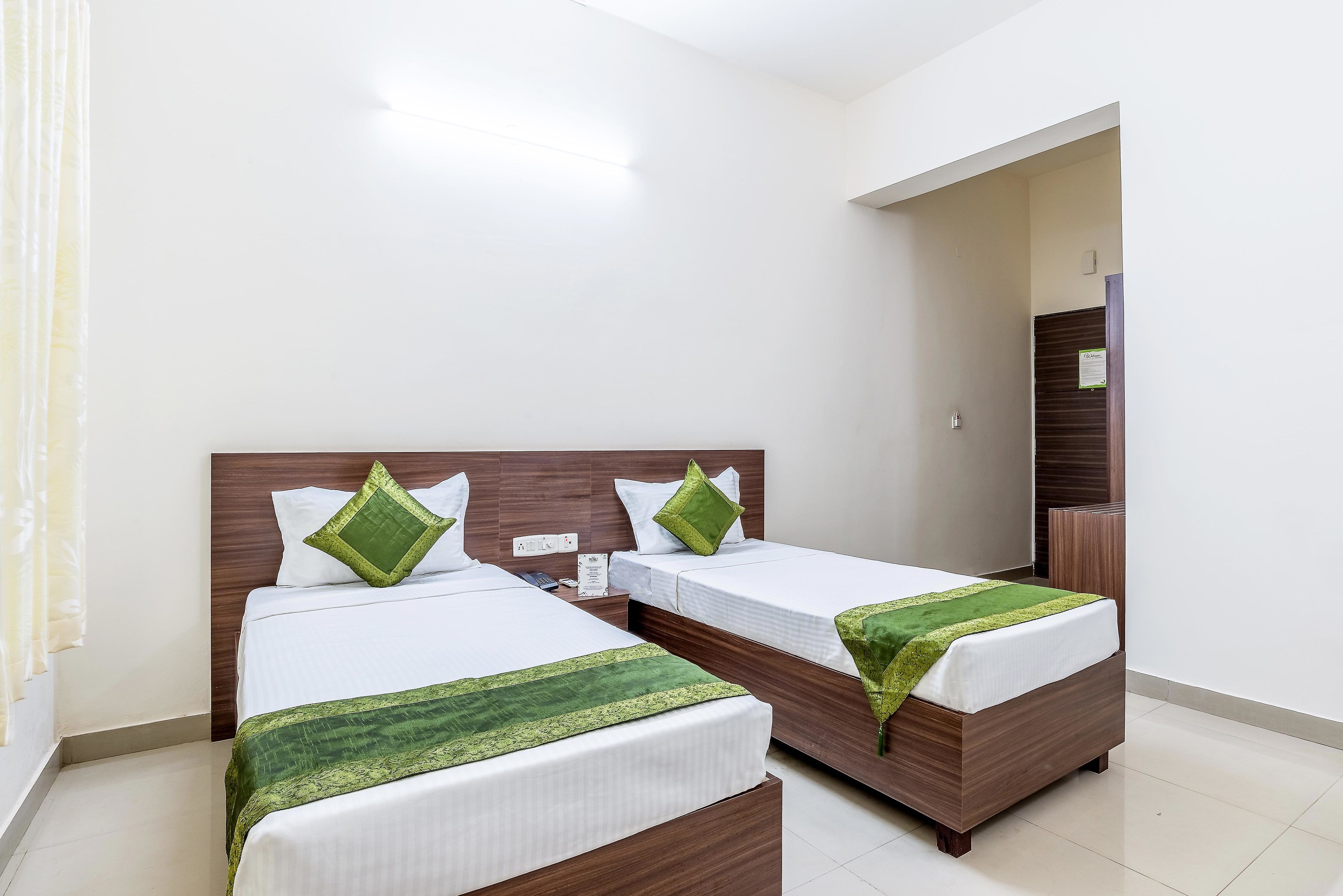 Una habitación de hotel con dos camas, cada una con cabecero de madera y ropa blanca. Hay una manta verde sobre una de las camas.