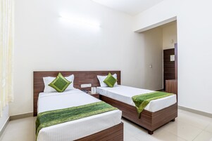 Una habitación de hotel con dos camas, cada una con cabecero de madera y ropa blanca. Hay una manta verde sobre una de las camas.