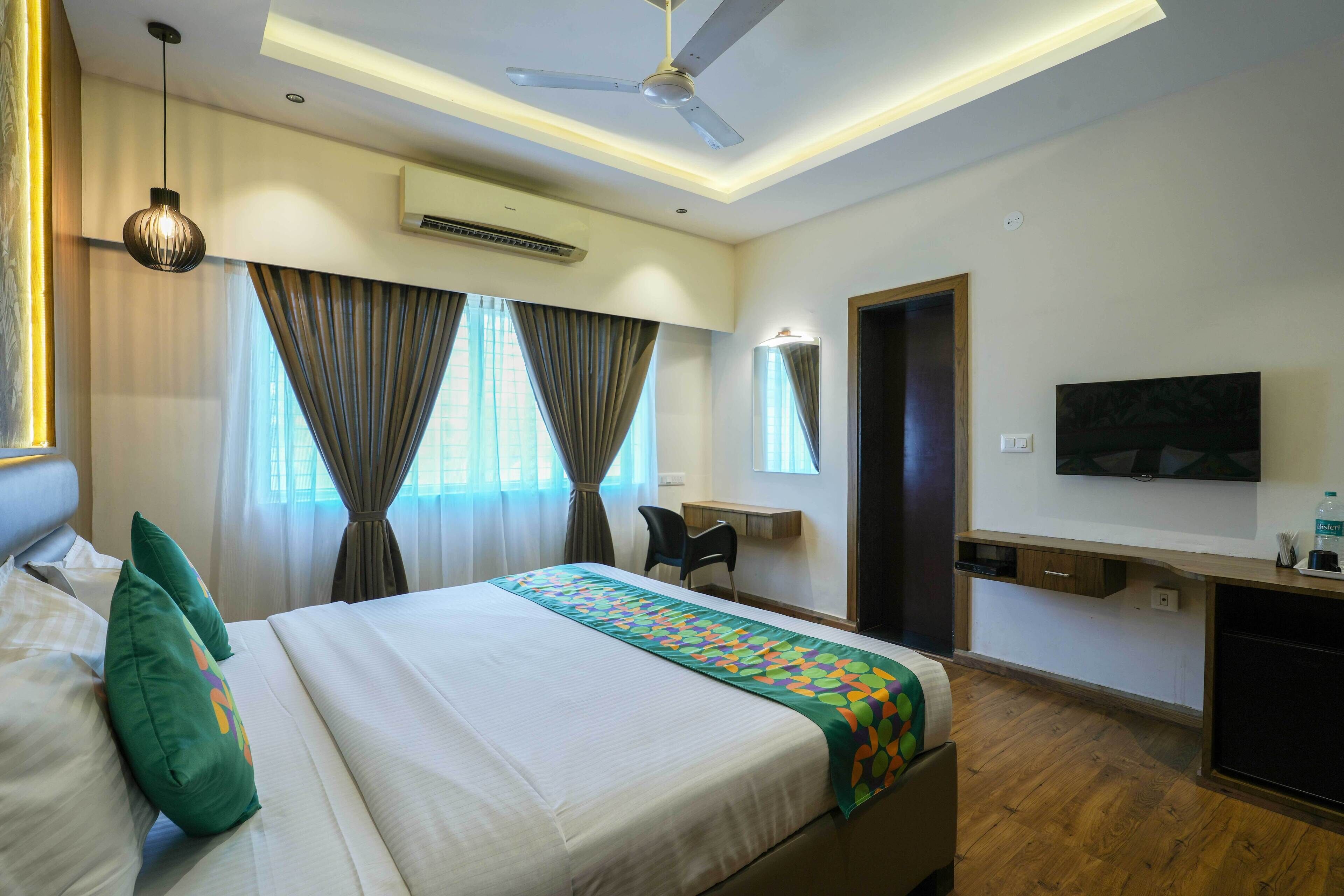 A hotel room with a bed, a desk, a chair, a TV, and a ceiling fan.
