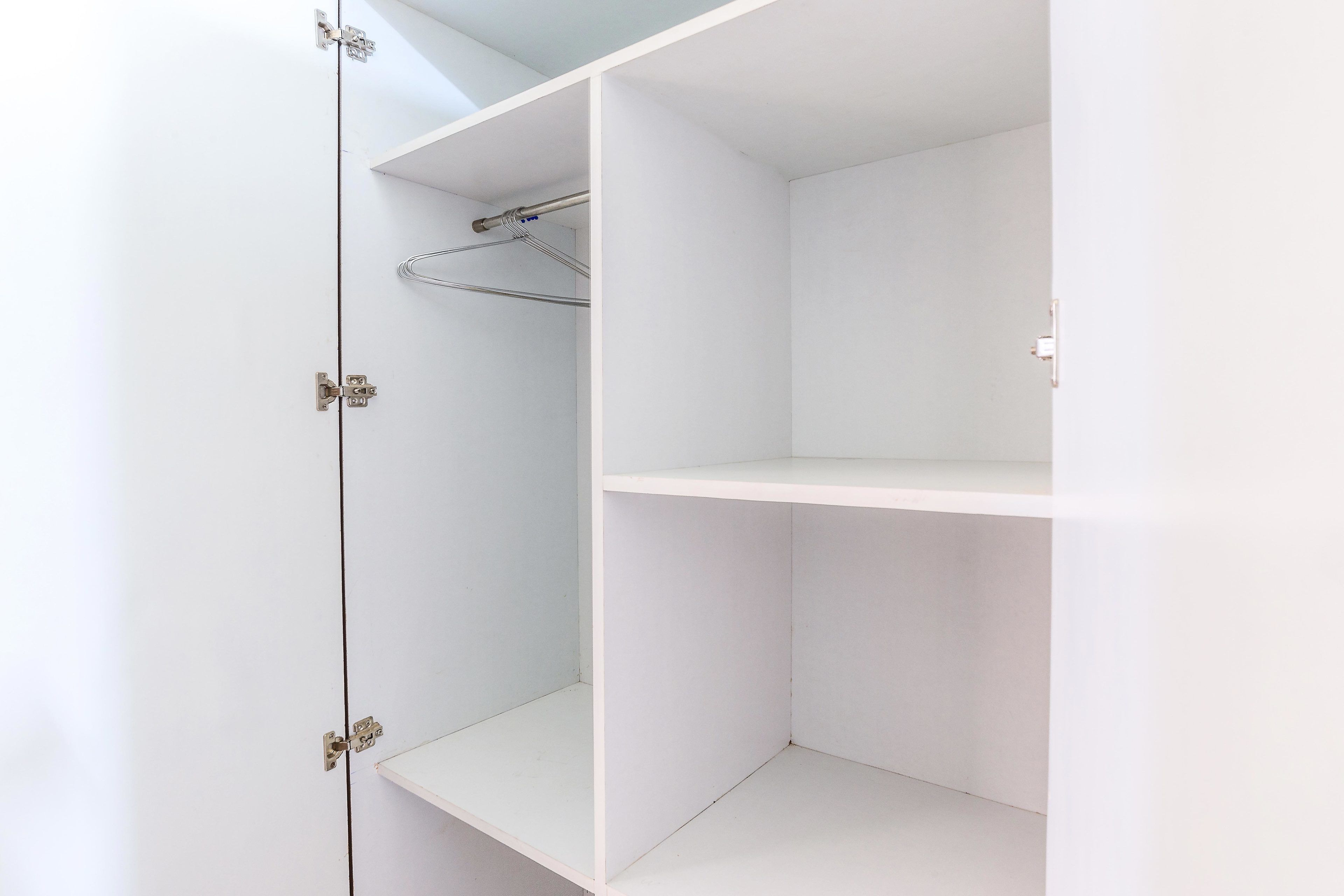 Un armario blanco con repisas abiertas y una barra para colgar ropa.