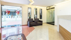 A reception area with a glass door, two dark-colored sofas, a reception desk, and a tiled floor. - Treebo Pappilon Palace - PVS Circle (Mangaluru)