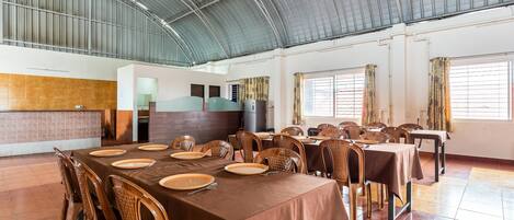 Un comedor amplio con techos altos y ventanas grandes, con varias mesas dispuestas para comer.