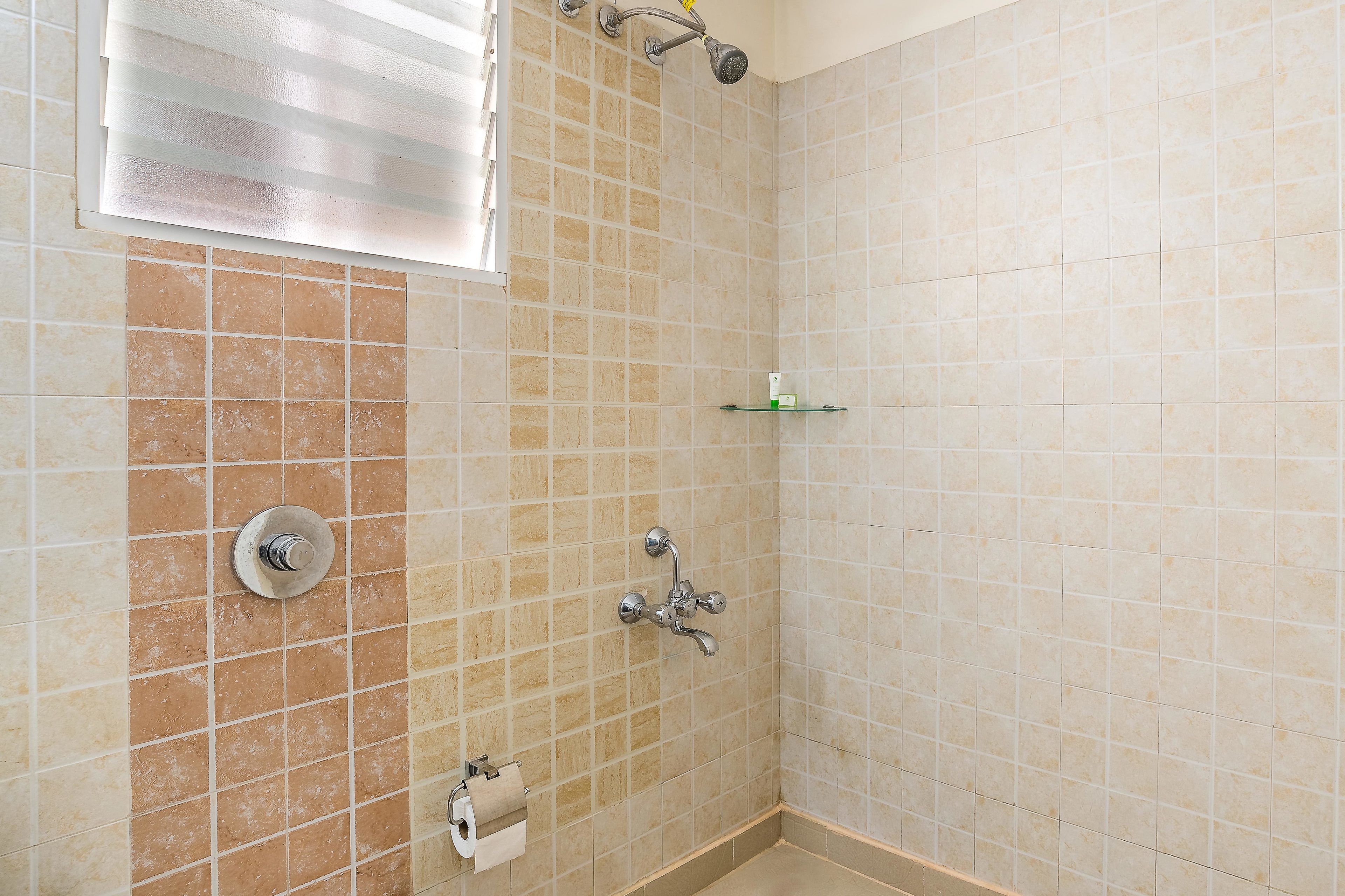 Um banheiro pequeno com azulejos, um chuveiro, um vaso sanitário e uma prateleira.