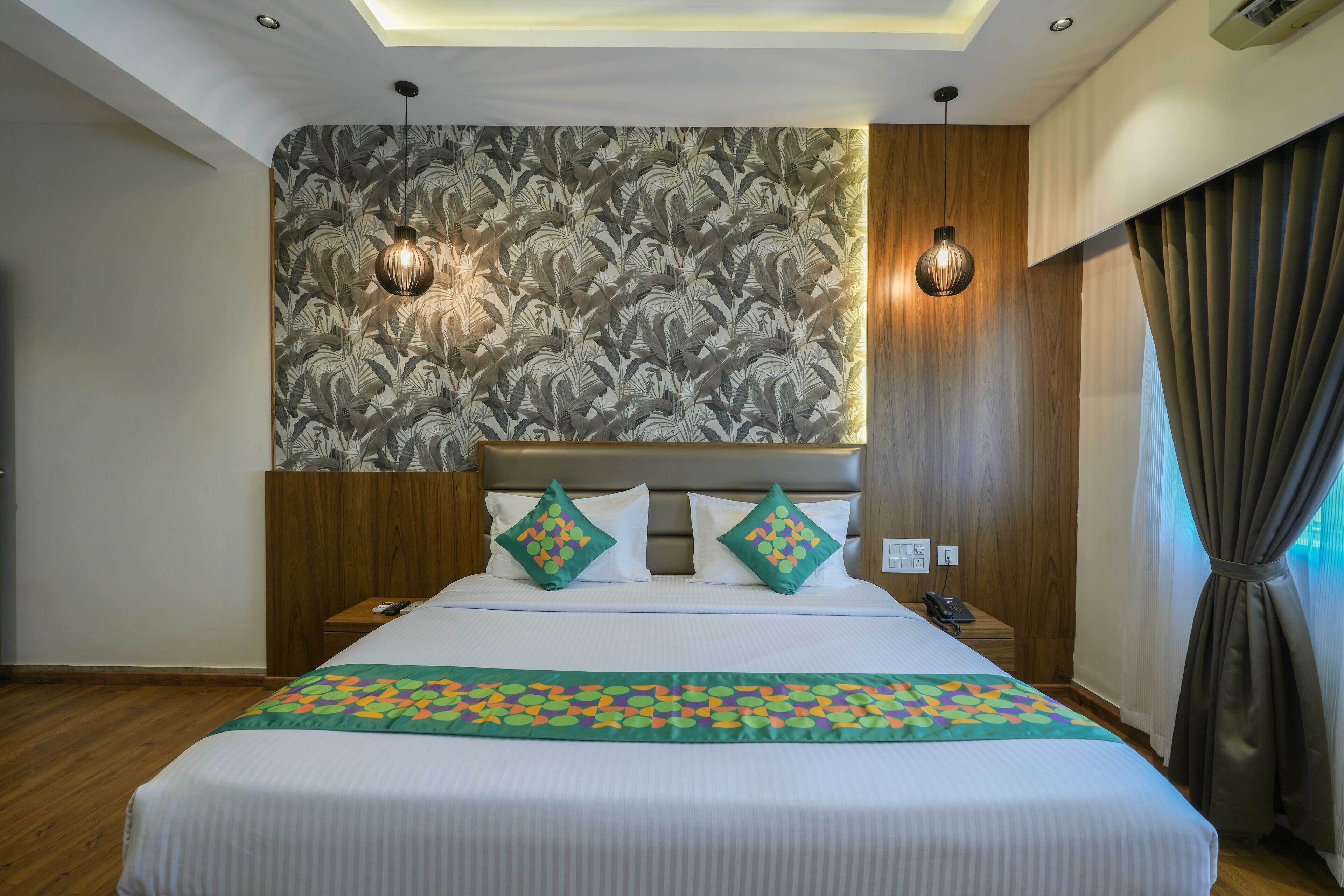 Een hotelkamer met een groot bed, twee bedlampjes, een patroonbehang en een houten hoofdbord.
