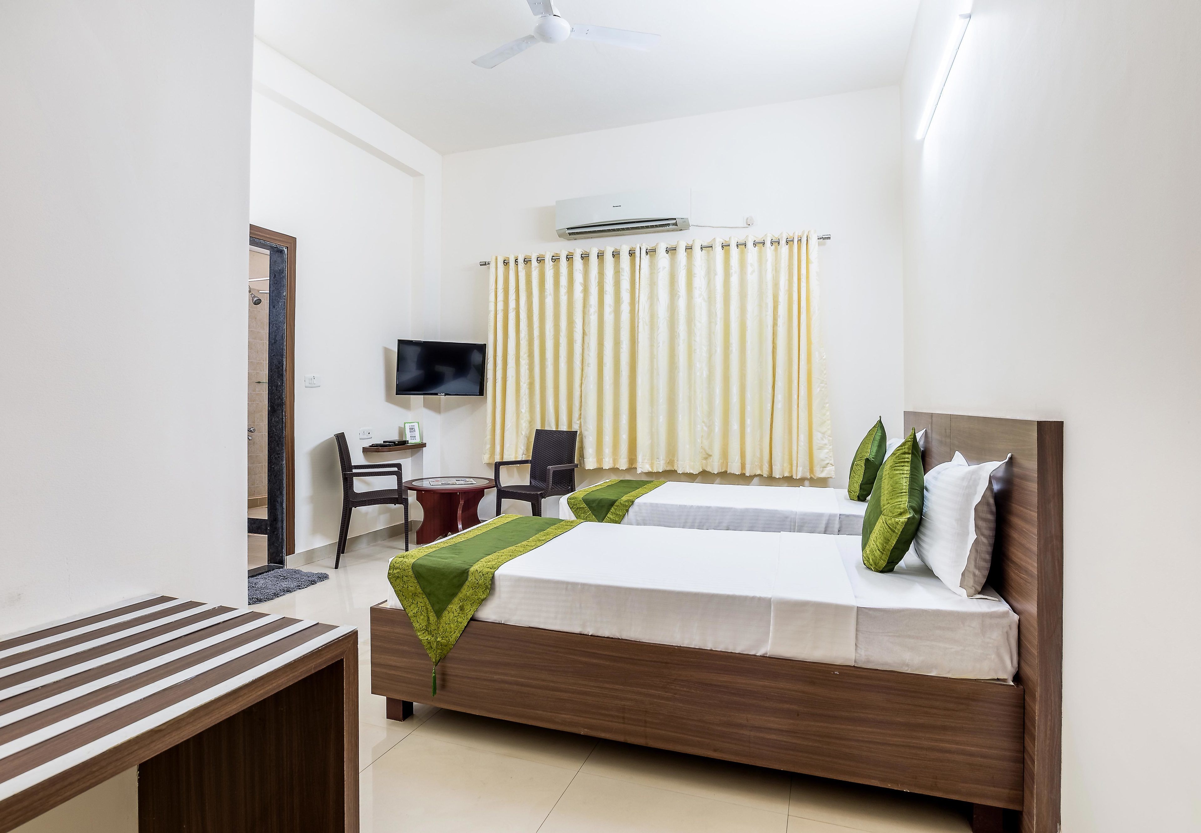 Quarto de hotel com duas camas, uma escrivaninha, uma cadeira, uma TV e um aparelho de ar condicionado.