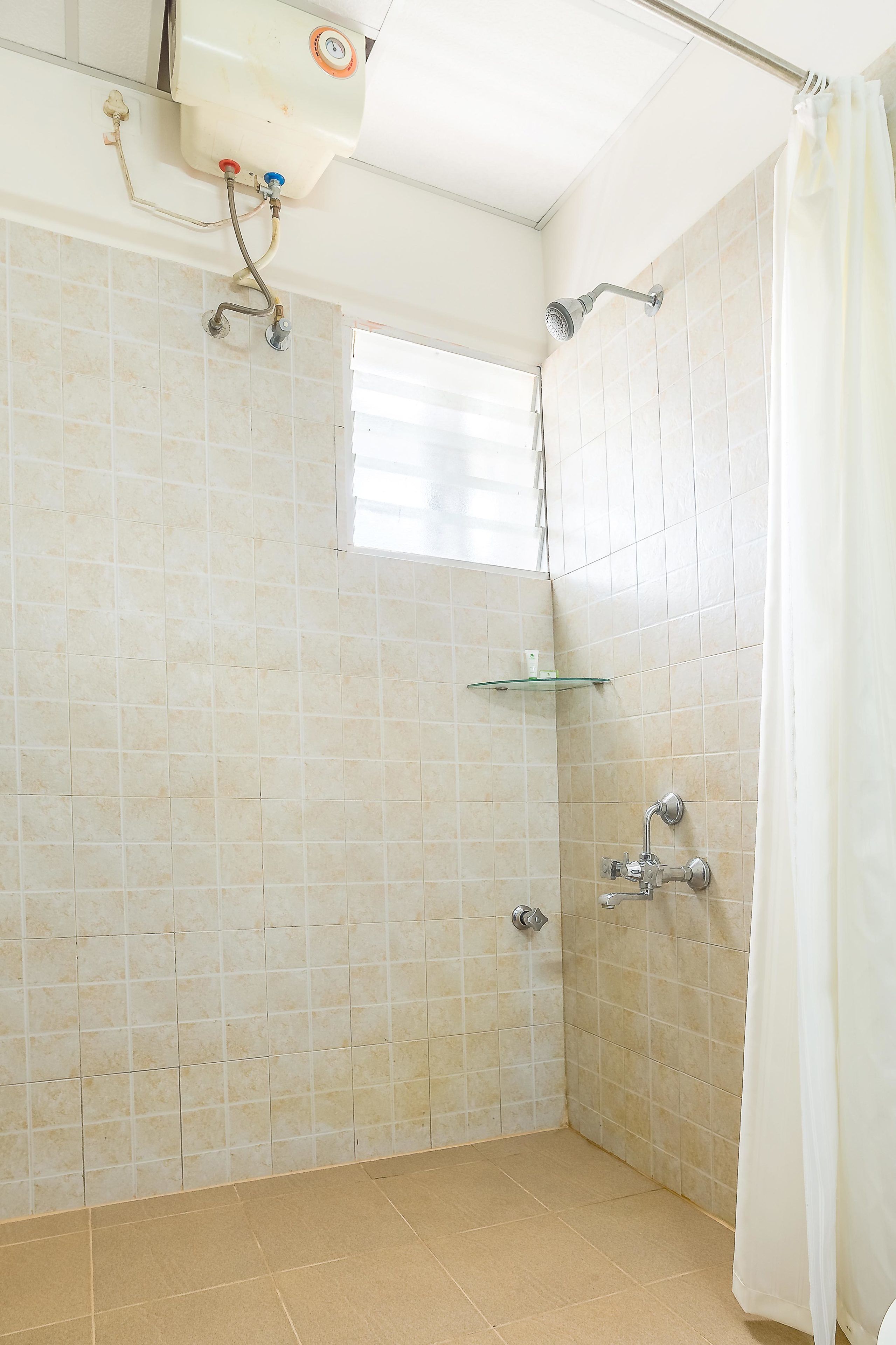 A small, tiled shower room with a glass shelf and a showerhead.