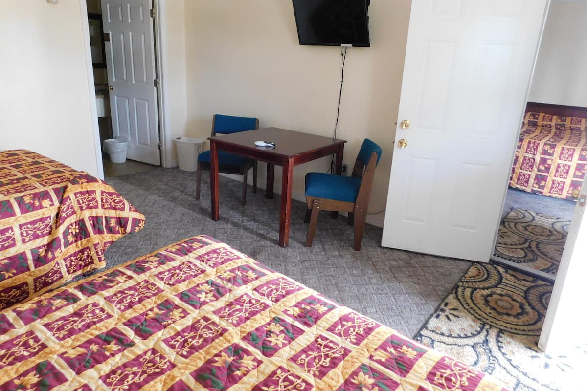 A room with a bed, a table, two chairs, a television mounted on the wall, and a door.