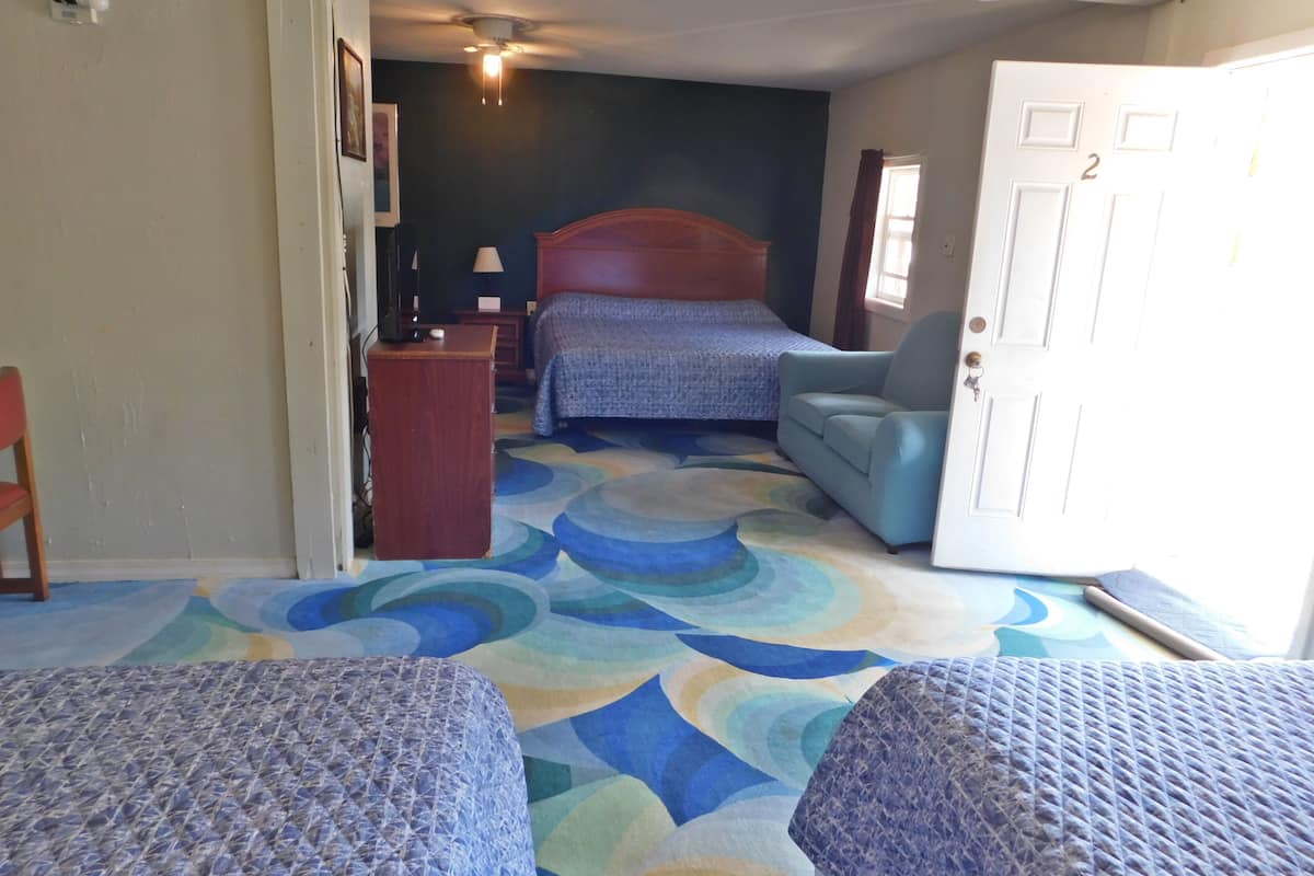 A hotel room with two beds, a desk, a chair, and a door.