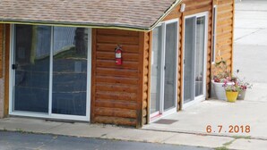 A small wooden cabin with a tiled roof, large sliding glass doors, and a fire extinguisher mounted on the wall. - Little Shamrock Motel A1 (Murfreesboro)