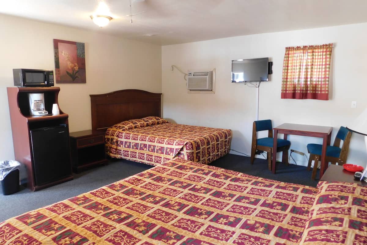 A hotel room with two beds, a desk, a chair, a television, a microwave, and a coffee maker.