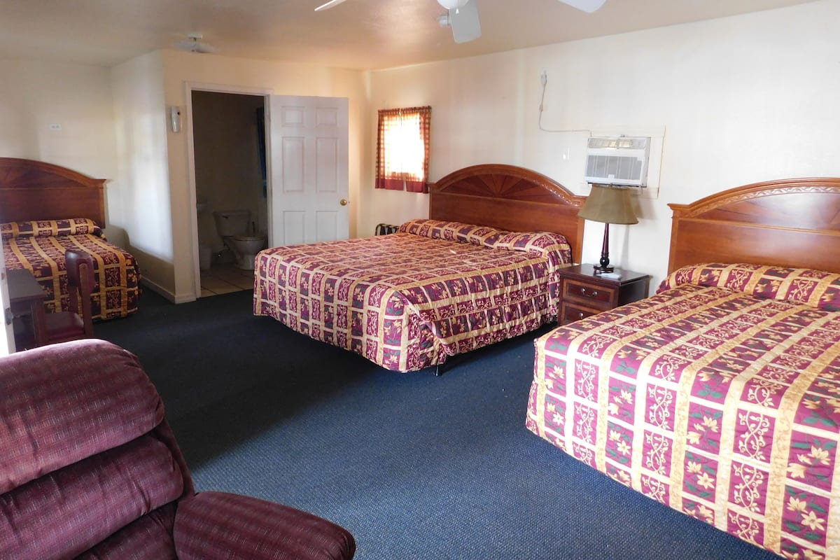A hotel room with two beds, a ceiling fan, a nightstand with a lamp, and a chair.