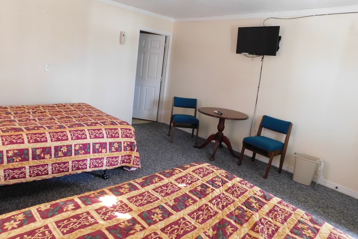 A room with two beds, a small table, two chairs, a television, and a door.