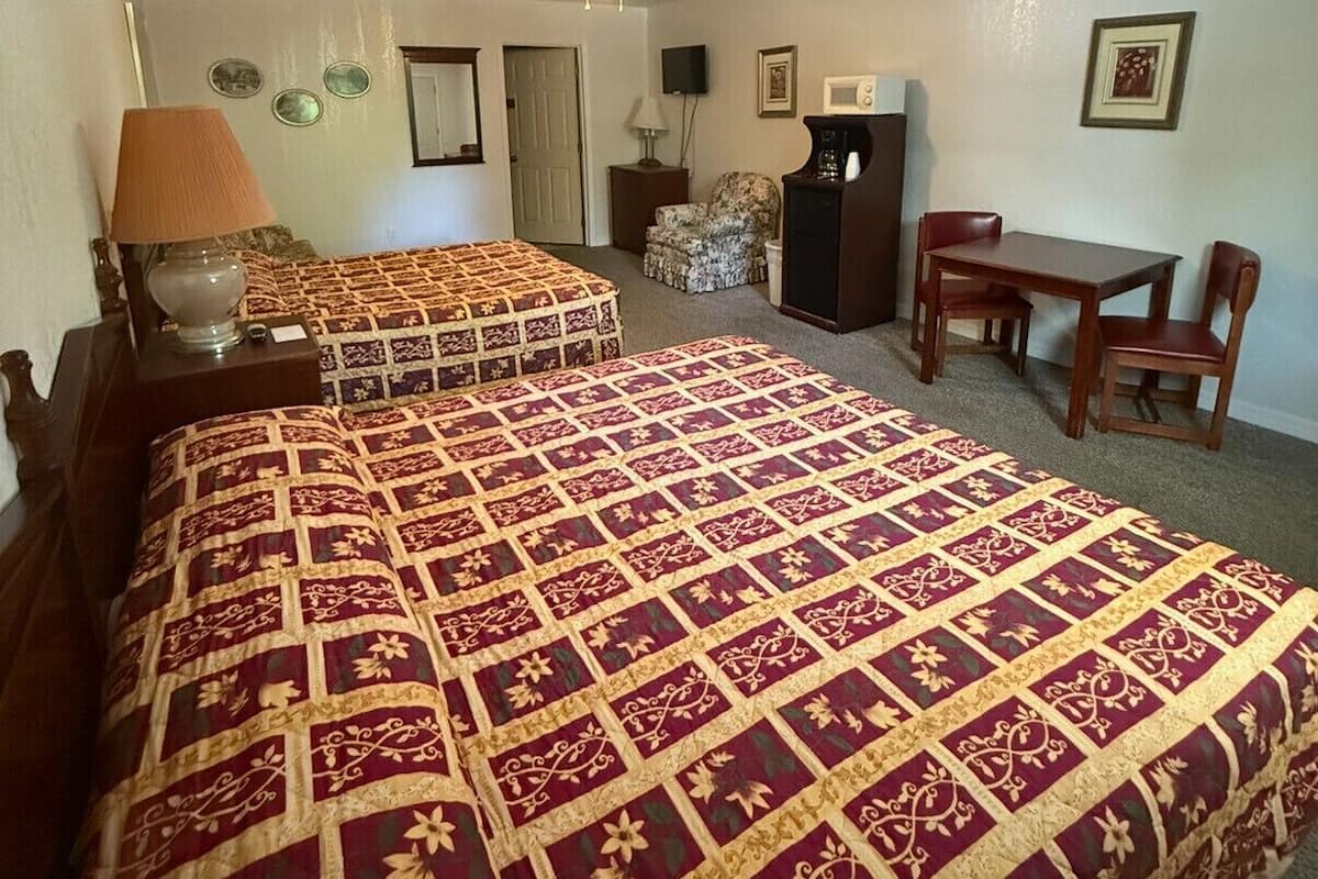 A hotel room with two beds, a desk, a chair, a television, and a ceiling fan.