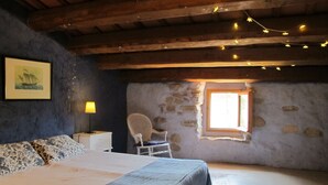 Un dormitorio con cama, una silla, una mesita, una lámpara y una ventana con vistas al exterior.