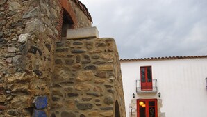 Un muro de piedra con una puerta roja y un balcón con barandilla roja.