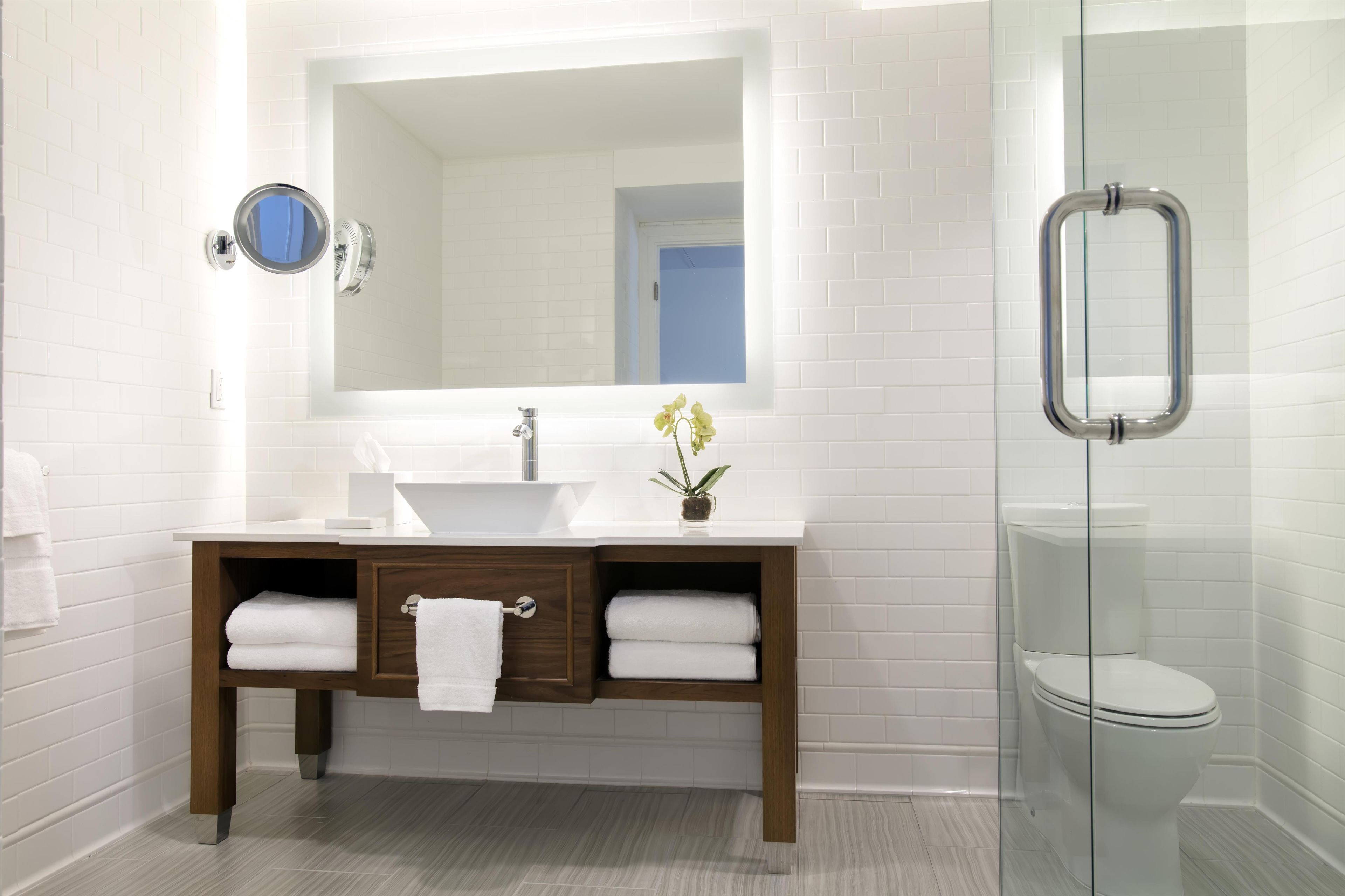 Un bagno moderno con un lavandino bianco, un mobile bagno in legno, uno specchio e un box doccia in vetro.