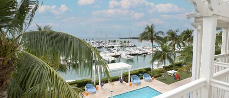 A pool area with a view of a marina filled with boats, surrounded by palm trees and a white gazebo.