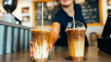 Two iced coffee drinks in clear plastic cups with lids and straws, held by a person.