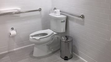 A modern bathroom with a white toilet, a handrail, and a trash bin.