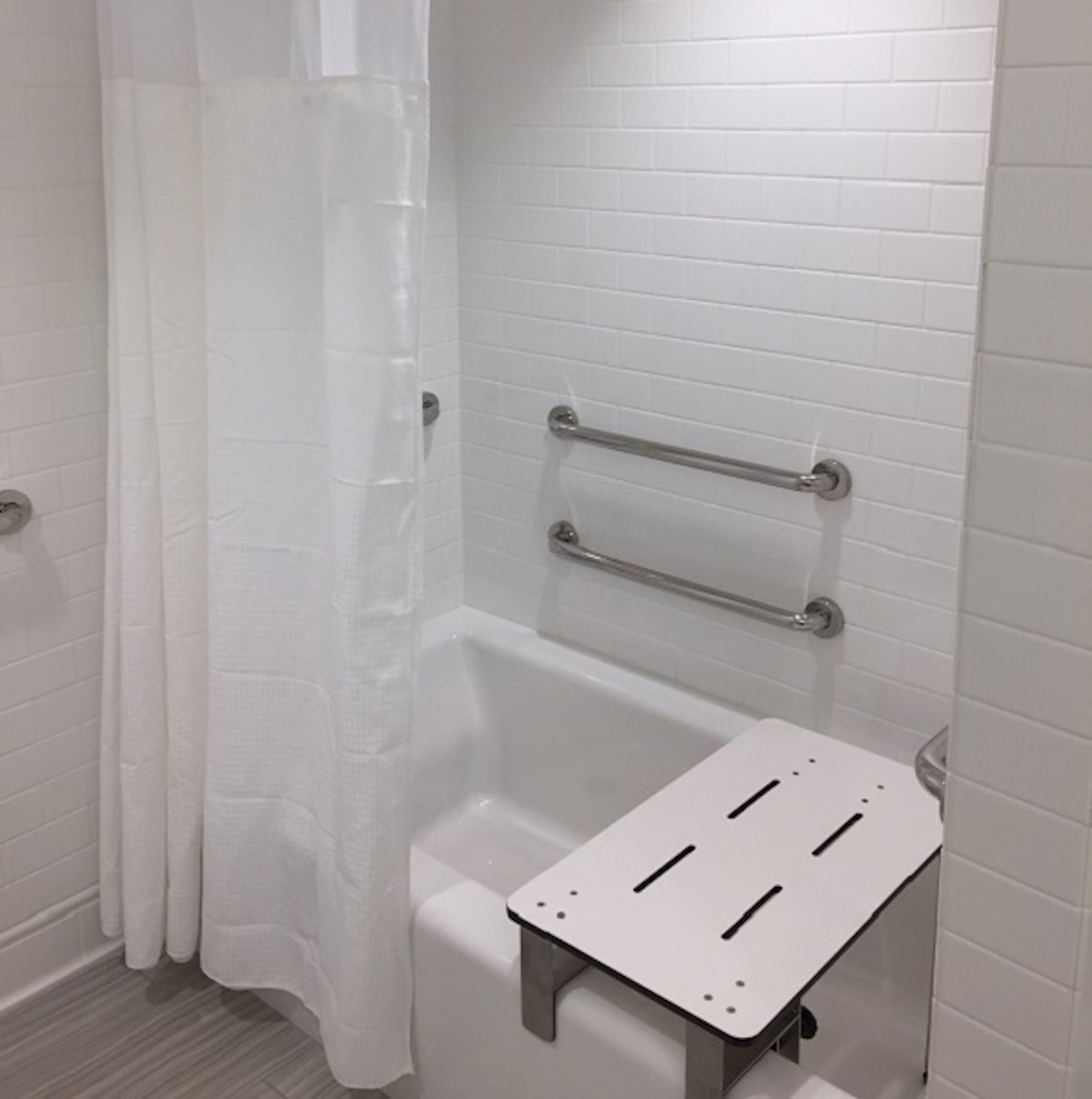 Une salle de bain avec une baignoire blanche, un rideau de douche et une barre d’appui fixée au-dessus de la baignoire.